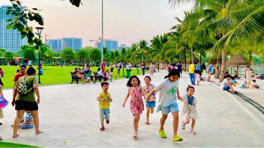 Hình ảnh người dân, gia đình và trẻ em vui chơi trong khu công viên có lối đi bộ, thảm cỏ và không gian xanh. Phù hợp với phần phân tích nhu cầu ở thực, chất lượng cuộc sống và giá trị sử dụng của bất động sản khu Đông.